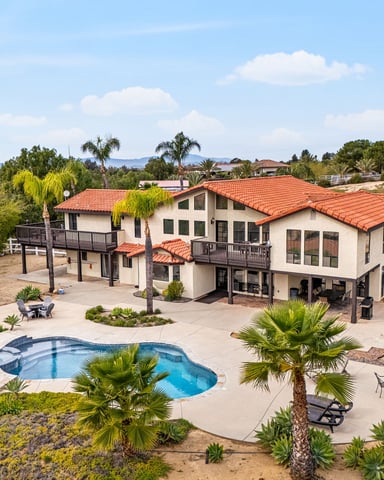 Open-plan kitchen, dining, and living area with white cabinetry, island seating, wood dining table, and expansive windows overlooking rolling hills.
